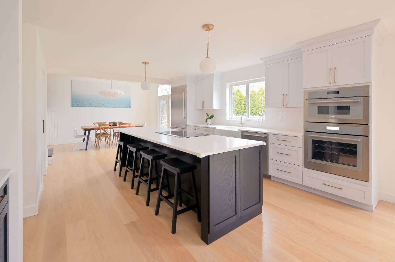 Bright modern kitchen with white cabinetry, black island seating, and light wood flooring